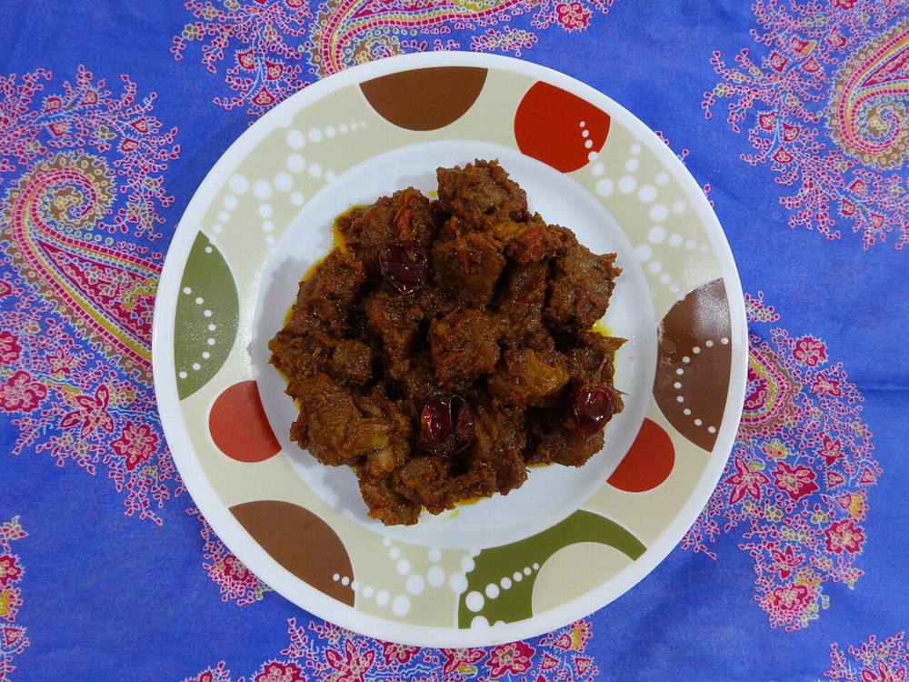 A bowl of home-cooked beef rendang, deep brown with visible shreds of toasted coconut