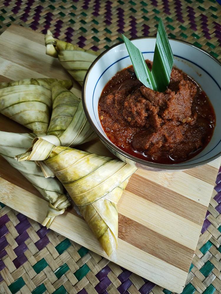 Rendang tok served with ketupat palas, the dark glossy Perak-style beef rendang