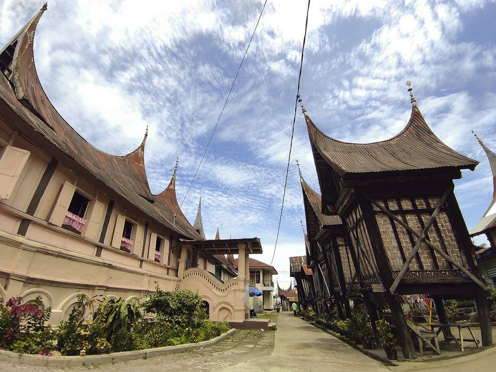A traditional rumah gadang with sweeping horn-shaped roof peaks, with small rangkiang rice barns in front